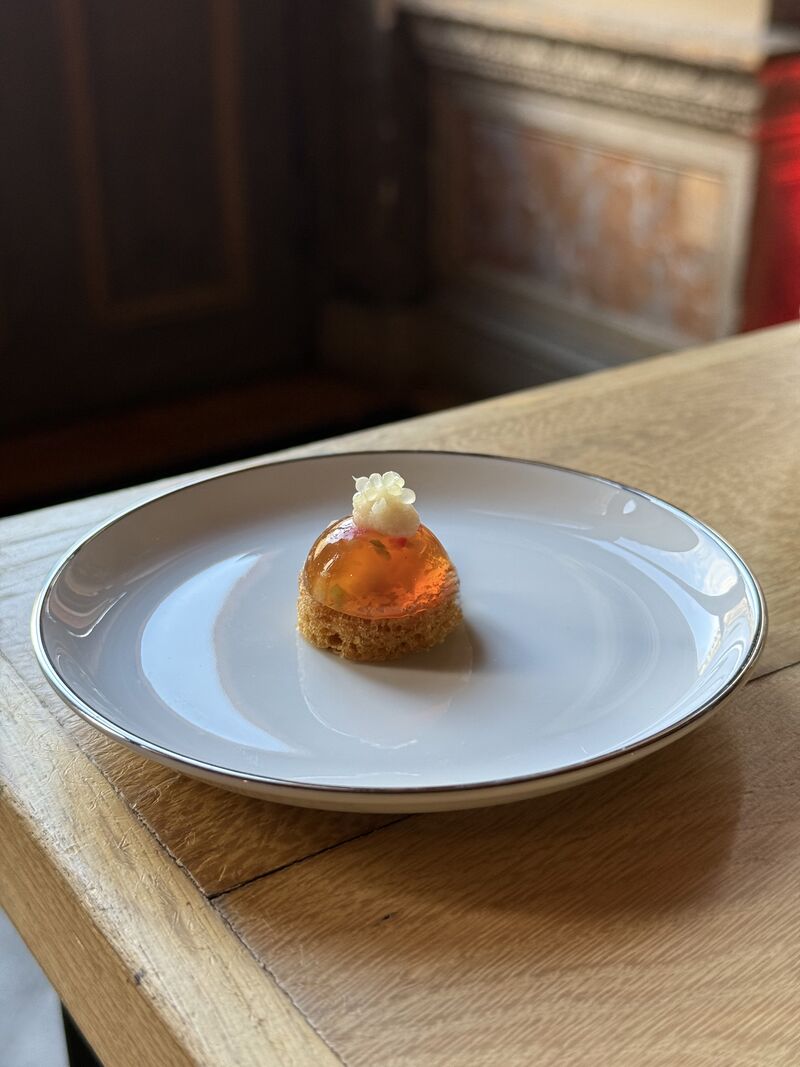 Une cheffe souriante en tenue blanche dresse une table élégante en extérieur avec des amuse-bouches, des plats colorés et des compositions florales, illustrant une expérience traiteur printanière raffinée et conviviale.