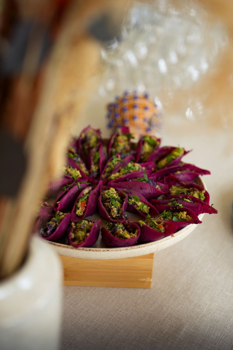 Une cheffe souriante en tenue blanche dresse une table élégante en extérieur avec des amuse-bouches, des plats colorés et des compositions florales, illustrant une expérience traiteur printanière raffinée et conviviale.