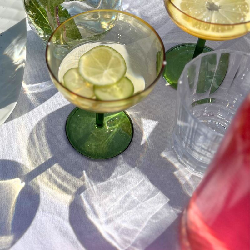 Une cheffe souriante en tenue blanche dresse une table élégante en extérieur avec des amuse-bouches, des plats colorés et des compositions florales, illustrant une expérience traiteur printanière raffinée et conviviale.