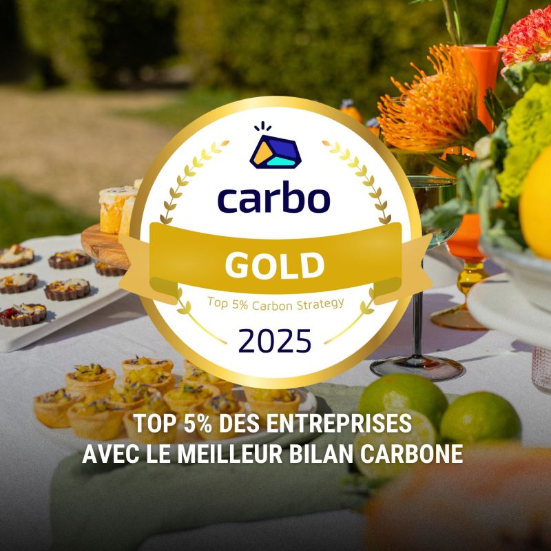 Une table extérieure élégante garnie de fruits frais, légumes de saison, pastèque, agrumes et bouchées apéritives, accompagnée de compositions florales colorées, illustrant une expérience traiteur printanière fraîche et conviviale.