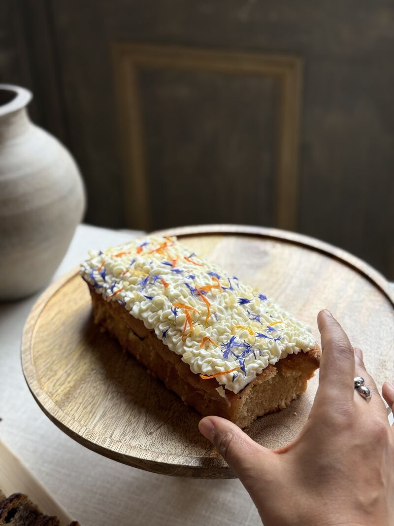 Une cheffe souriante en tenue blanche dresse une table élégante en extérieur avec des amuse-bouches, des plats colorés et des compositions florales, illustrant une expérience traiteur printanière raffinée et conviviale.
