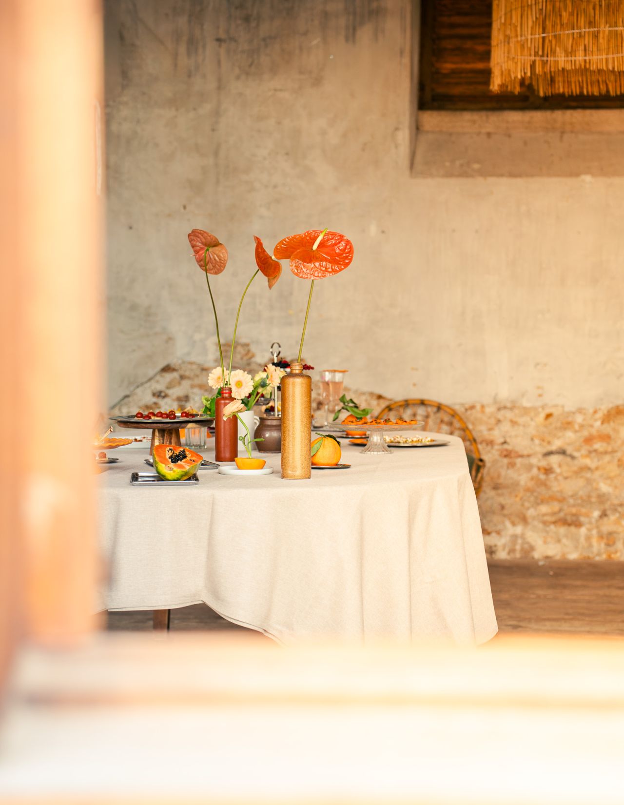 Une table extérieure élégante garnie de fruits frais, légumes de saison, pastèque, agrumes et bouchées apéritives, accompagnée de compositions florales colorées, illustrant une expérience traiteur printanière fraîche et conviviale.