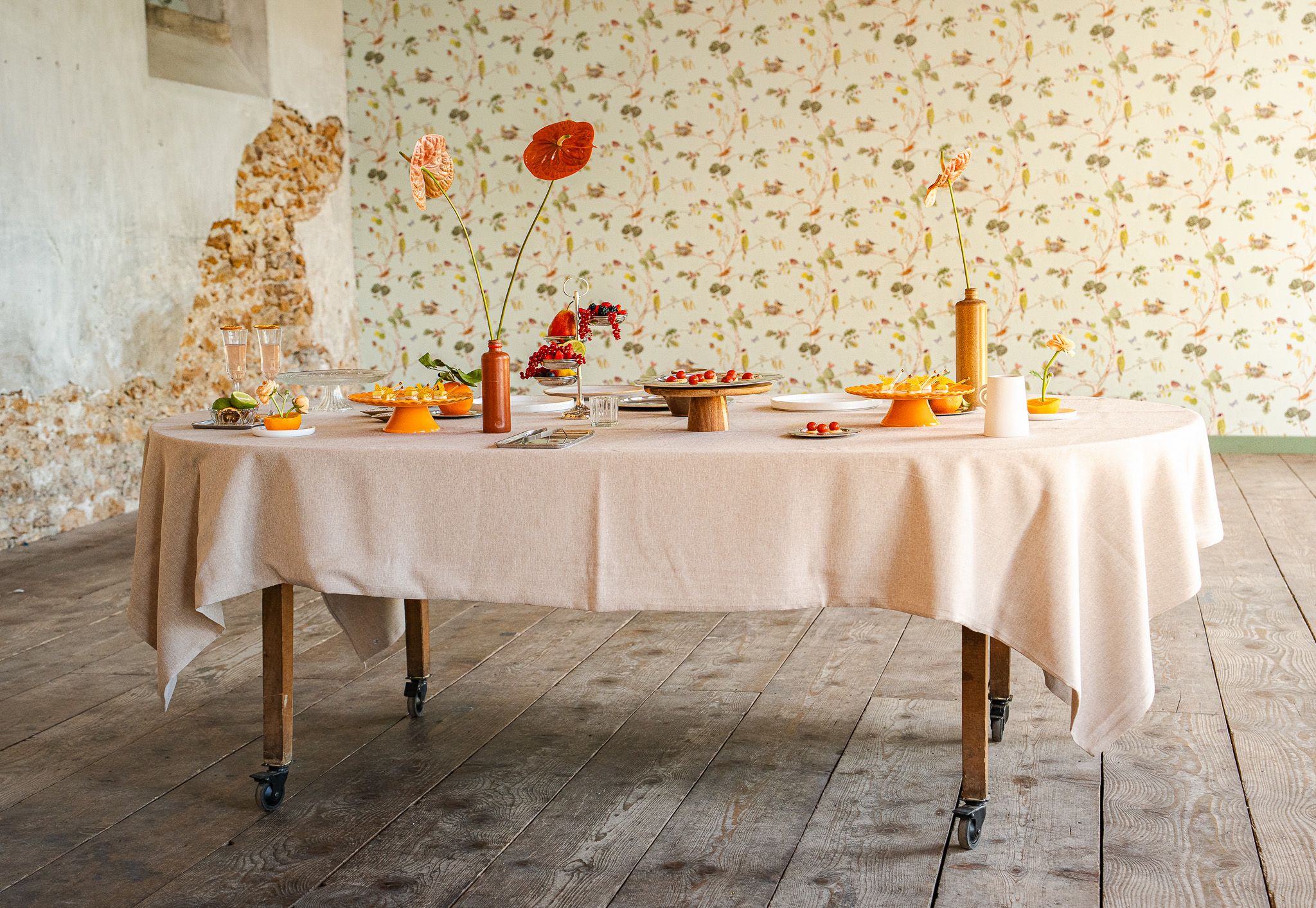 Une cheffe souriante en tenue blanche dresse une table élégante en extérieur avec des amuse-bouches, des plats colorés et des compositions florales, illustrant une expérience traiteur printanière raffinée et conviviale.