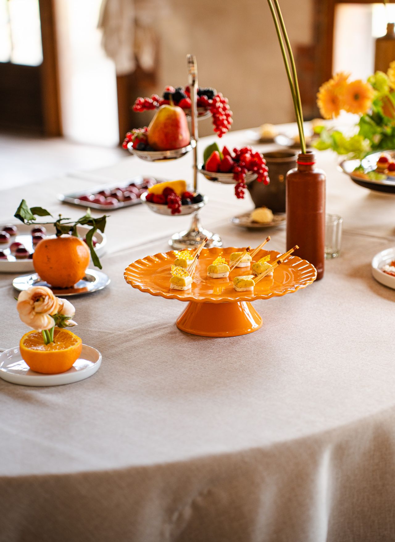 Une main verse une boisson rose rafraîchissante dans un verre sur une table élégante en extérieur, entourée de fruits, de fleurs et de plats colorés, illustrant une ambiance conviviale et estivale.