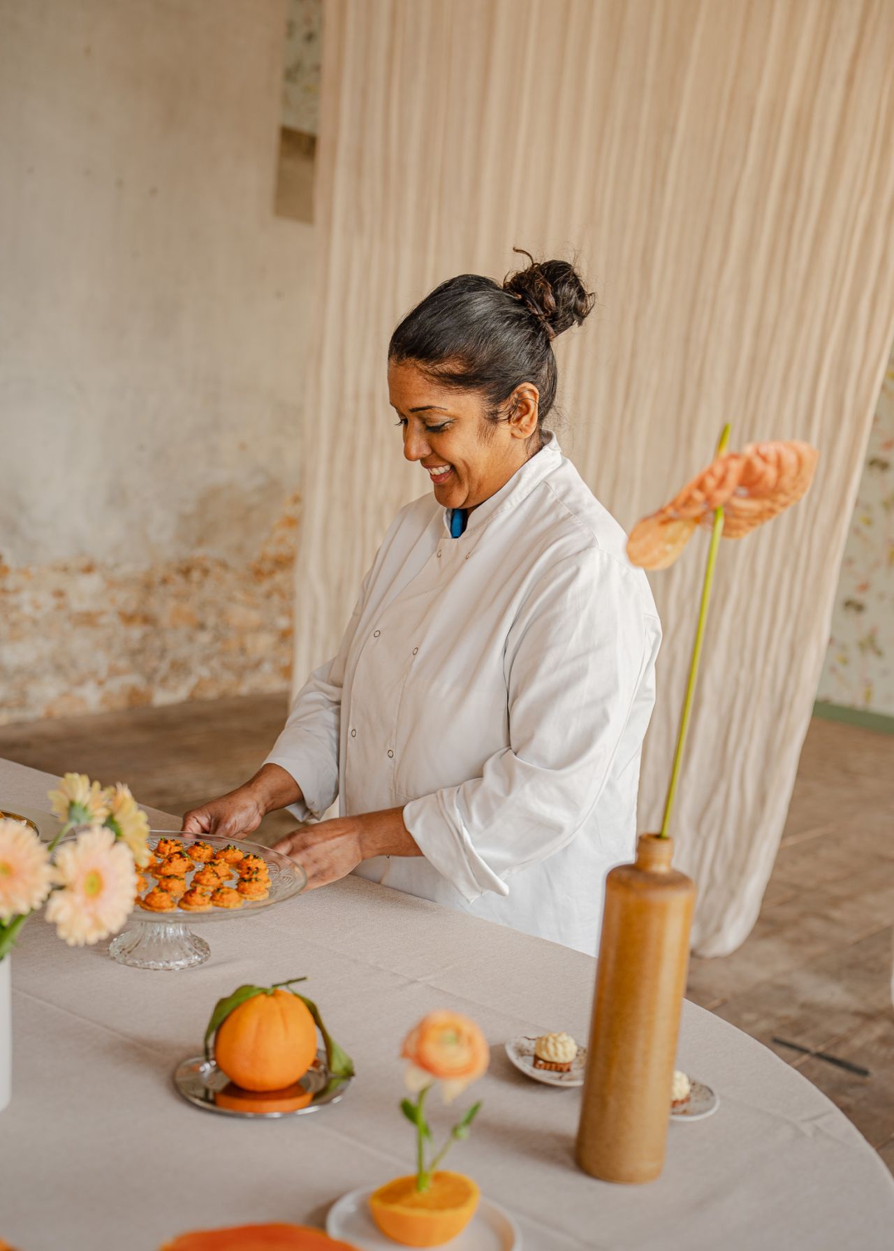 Une table extérieure élégante garnie de fruits frais, légumes de saison, pastèque, agrumes et bouchées apéritives, accompagnée de compositions florales colorées, illustrant une expérience traiteur printanière fraîche et conviviale.