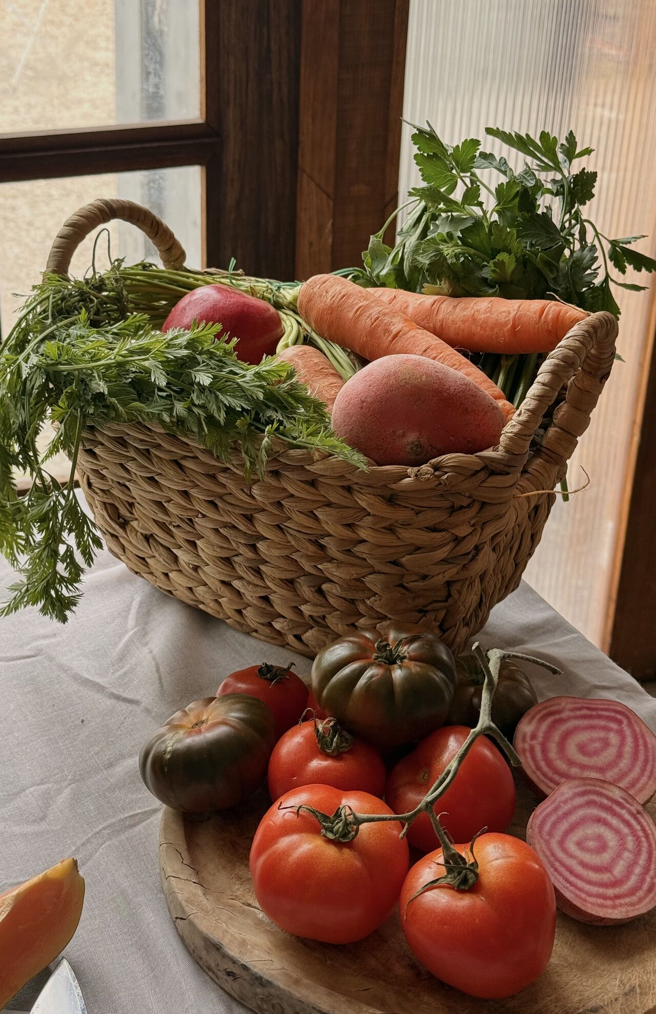 Une cheffe souriante en tenue blanche dresse une table élégante en extérieur avec des amuse-bouches, des plats colorés et des compositions florales, illustrant une expérience traiteur printanière raffinée et conviviale.