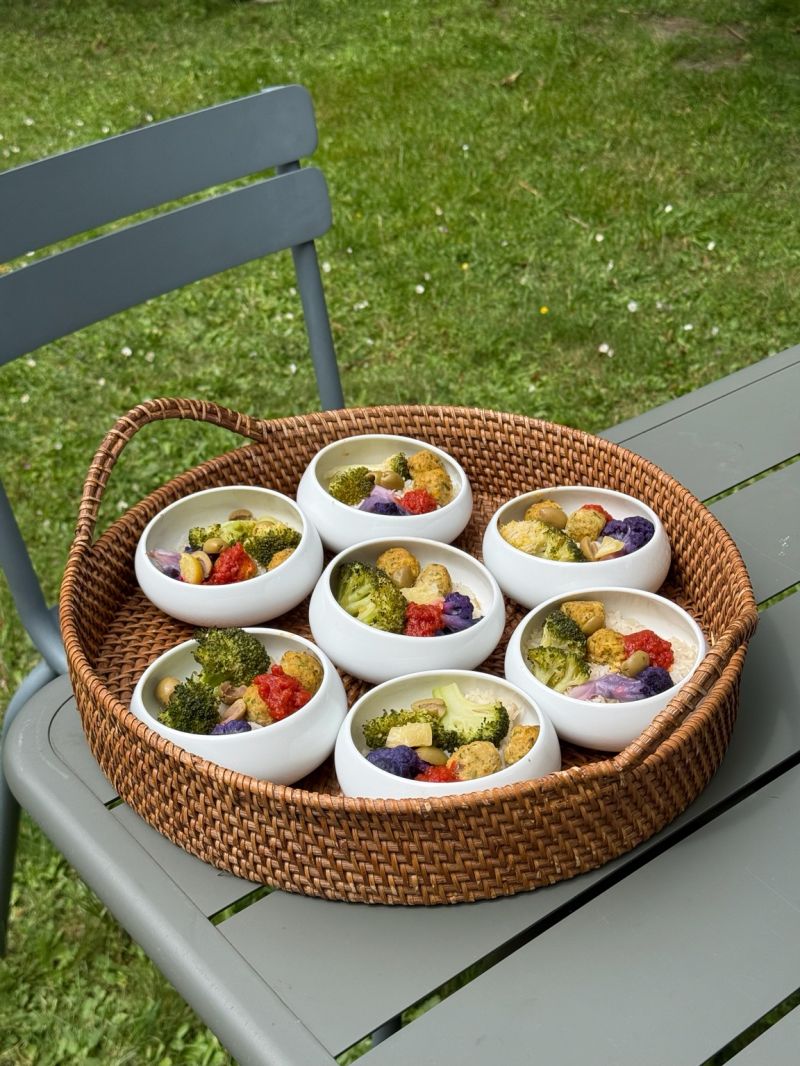 Une table extérieure élégante garnie de fruits frais, légumes de saison, pastèque, agrumes et bouchées apéritives, accompagnée de compositions florales colorées, illustrant une expérience traiteur printanière fraîche et conviviale.