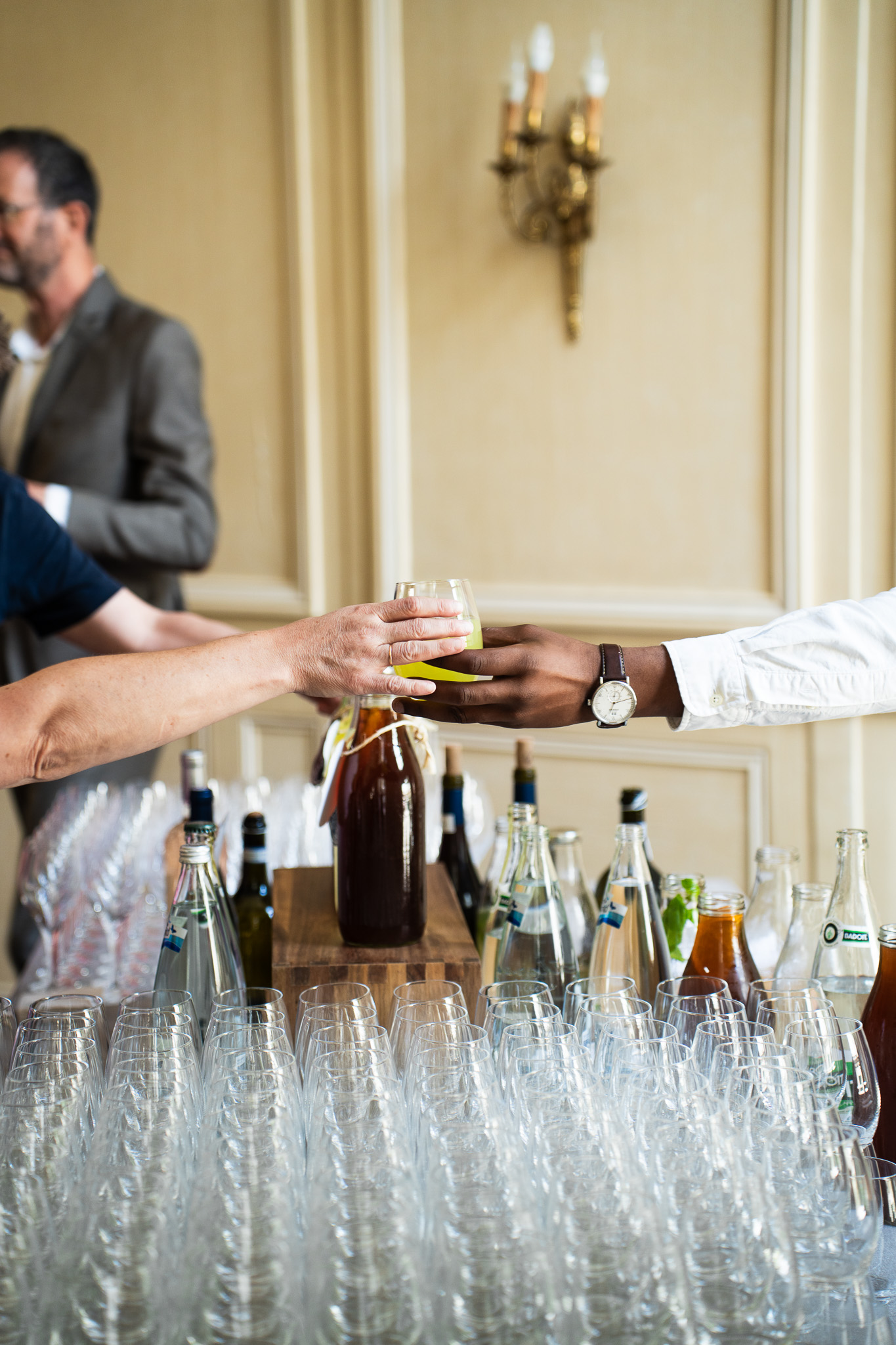 Une main utilise une pince pour ajuster délicatement des bouchées apéritives dorées disposées sur un présentoir en bois, illustrant une préparation traiteur soignée et un souci du détail.