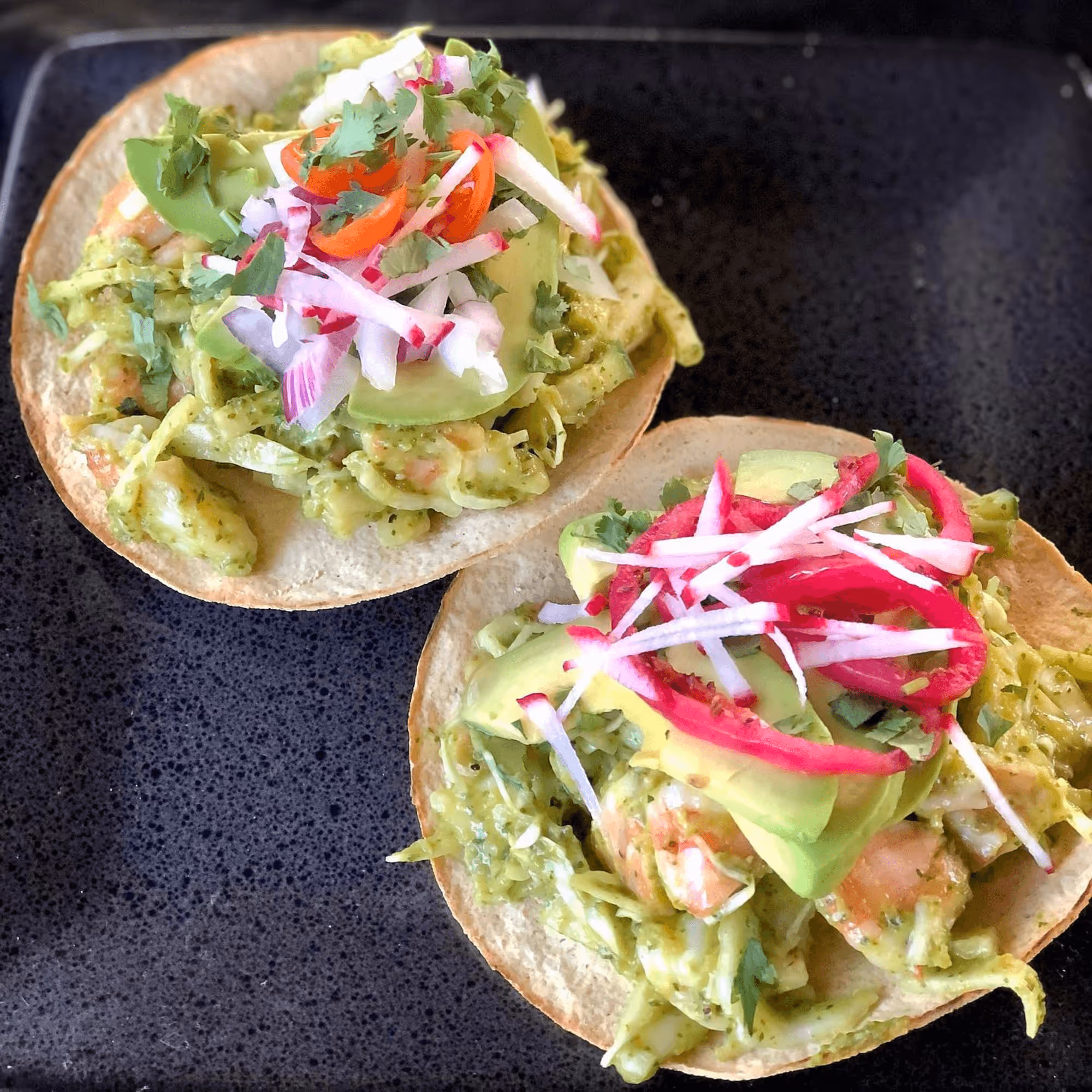 Two tacos with toppings on a black plate.