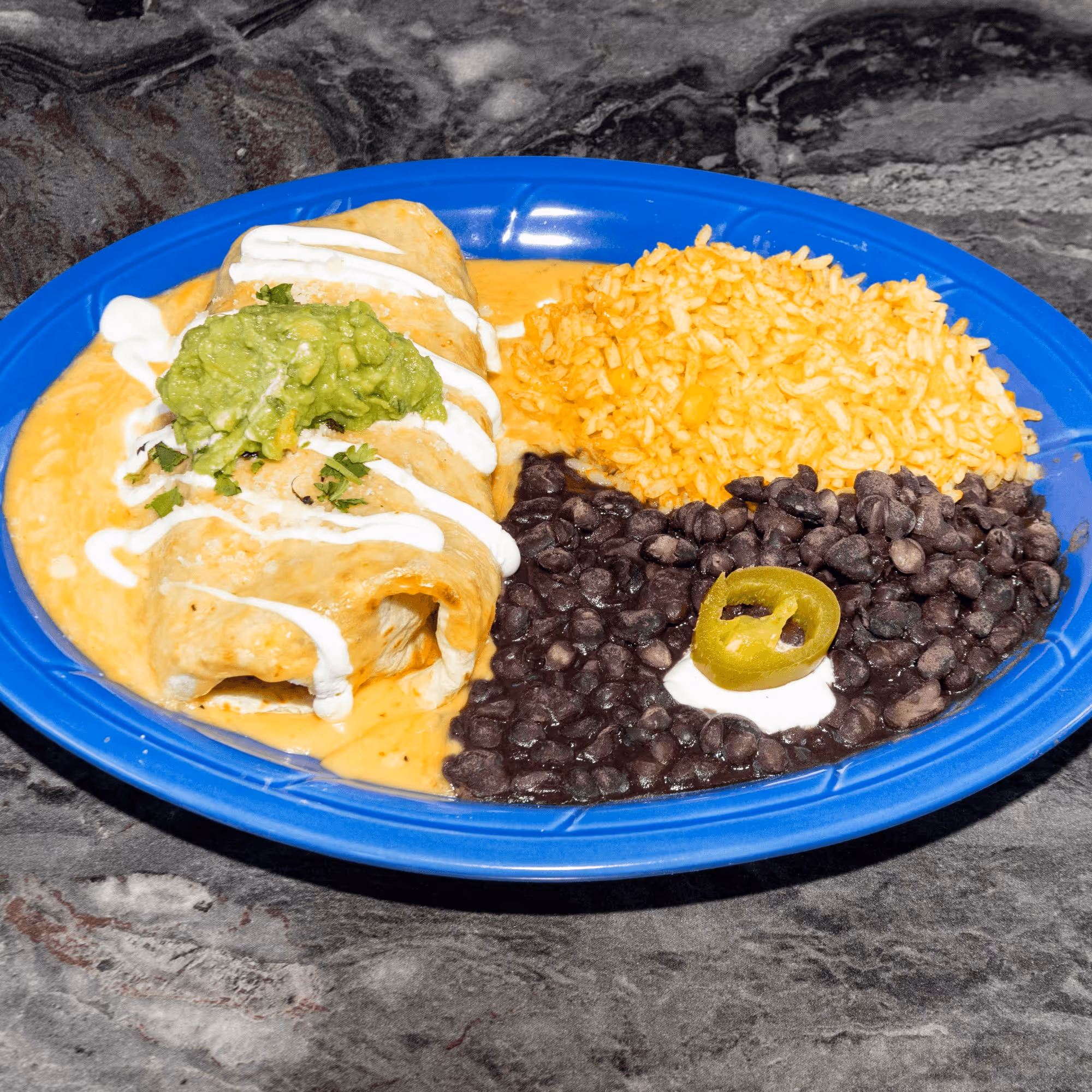A plate of food with a green pepper, beans, rice, and a burrito.