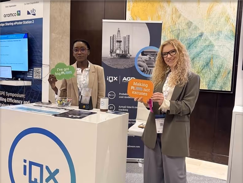 Two women standing at an iQX booth holding speech bubble signs, one reading 'I've got big PLANS' and the other 'Making PLans not excuses.'
