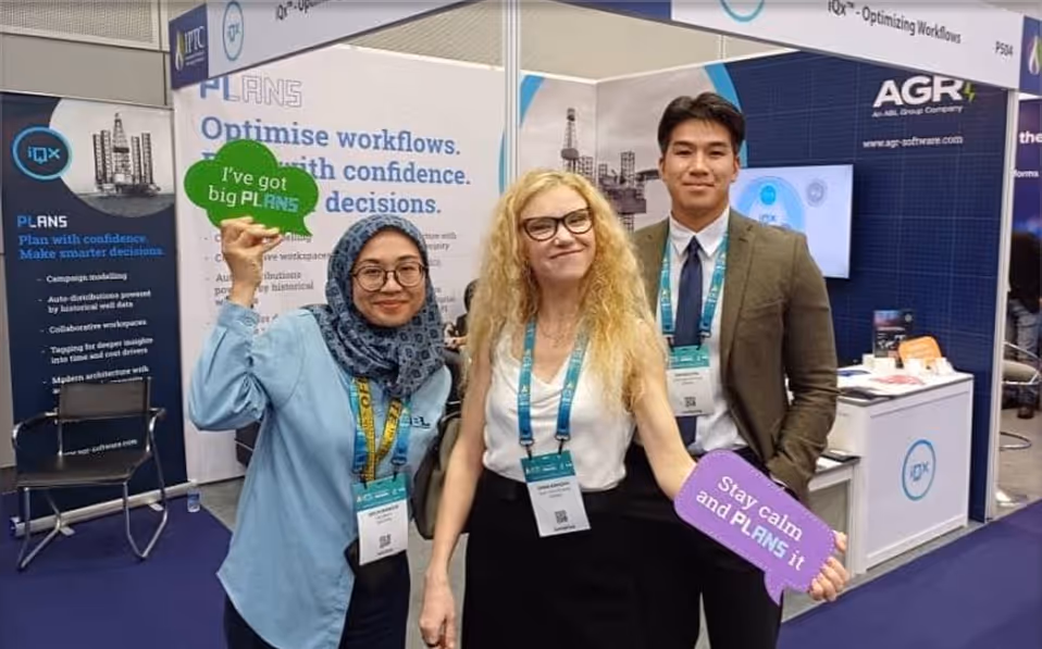 Three diverse conference attendees posing with speech bubble signs that say 'I've got big PLANS' and 'Stay calm and PLANS it' in a trade show booth.