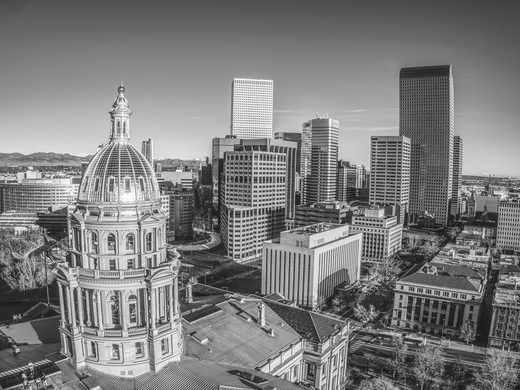 Black and white aerial view of a city skyline featuring a prominent domed capitol building with surrounding modern high-rise buildings.