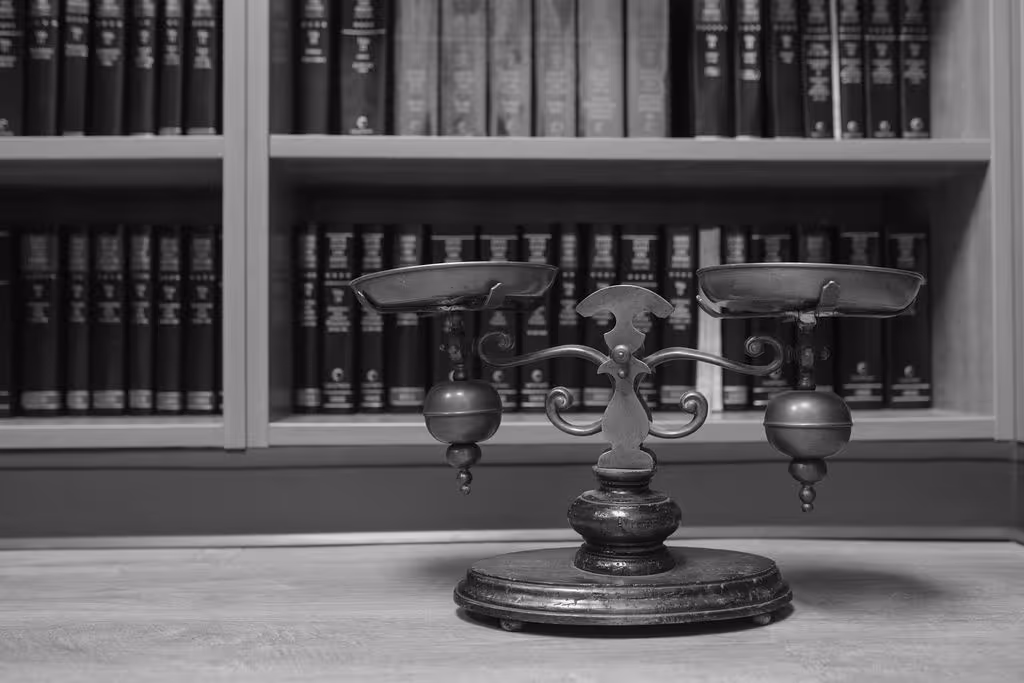 Antique balance scale on a wooden table with bookshelves filled with legal books in the background.
