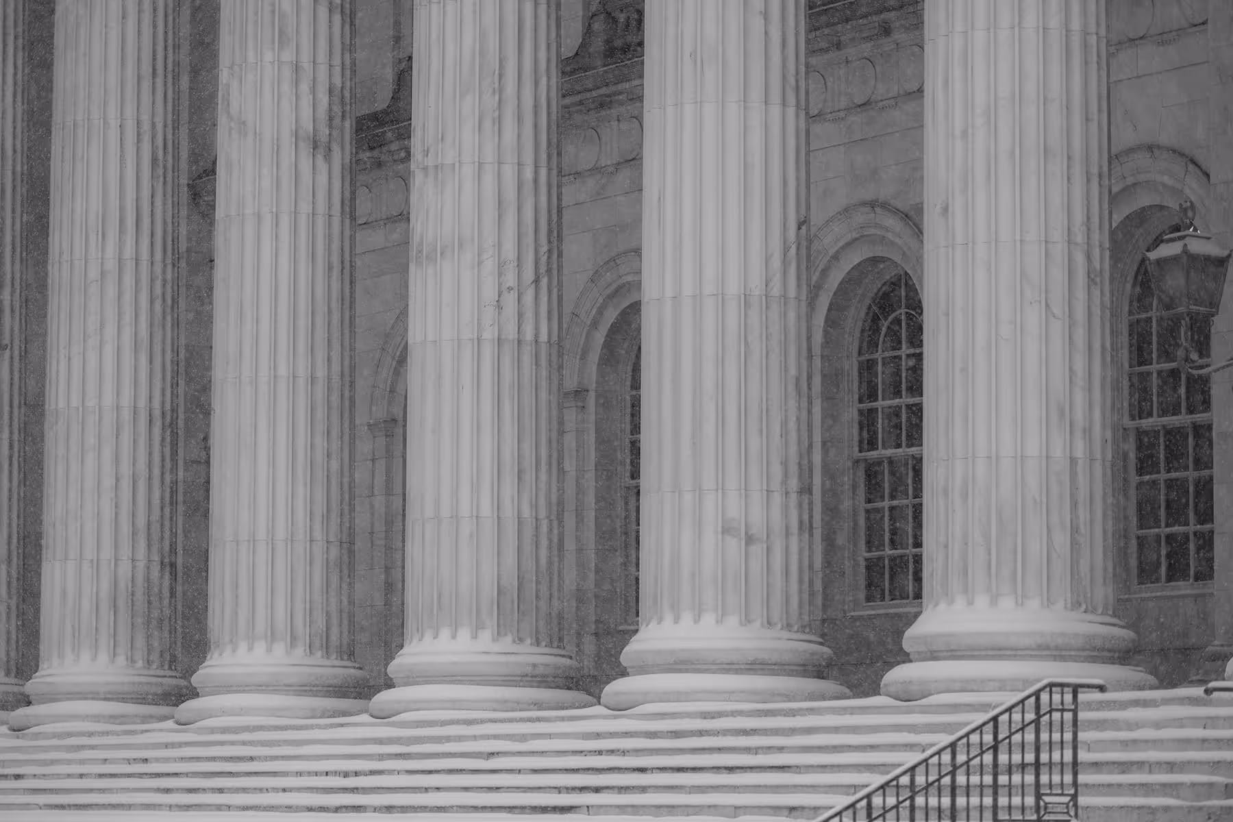 Snow-covered steps and large marble columns at the front entrance of a classical building.