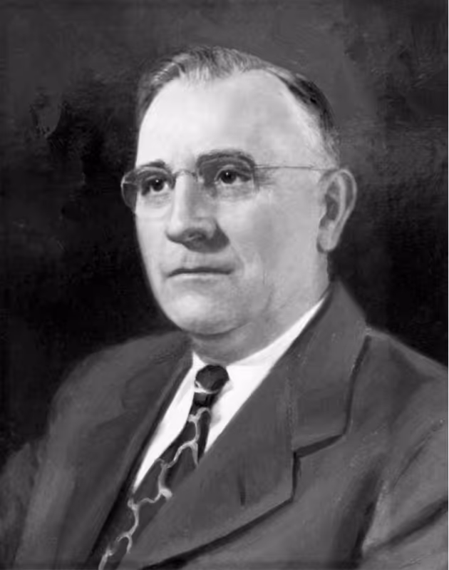 Black and white portrait of an older man wearing glasses, a suit jacket, white shirt, and patterned tie.
