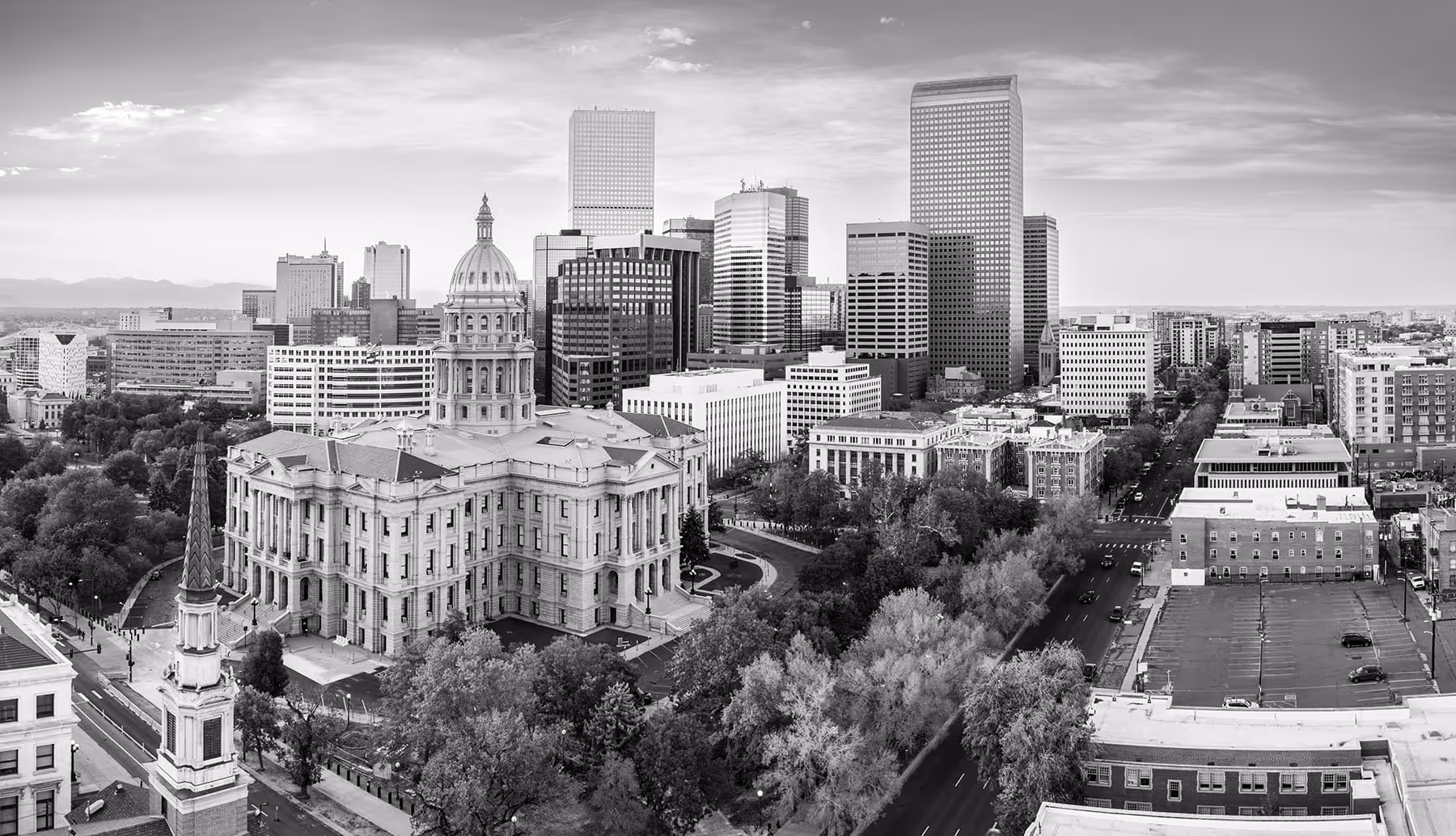 Aerial view of a cityscape featuring a historic capitol building with a dome surrounded by modern skyscrapers and tree-lined streets.