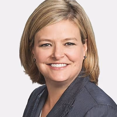 Smiling woman with short blonde hair wearing a dark pinstripe blazer against a plain light background.