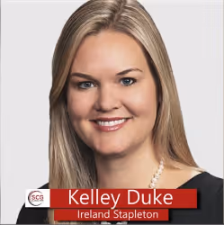 Portrait of Kelley Duke from Ireland Stapleton with blonde hair, smiling and wearing a black top and pearl necklace against a neutral background.