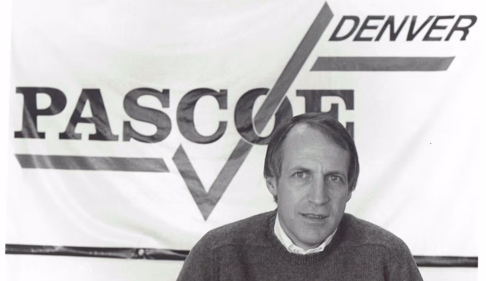 Black and white photo of a man in front of a banner with the words 'PASCOE DENVER.'