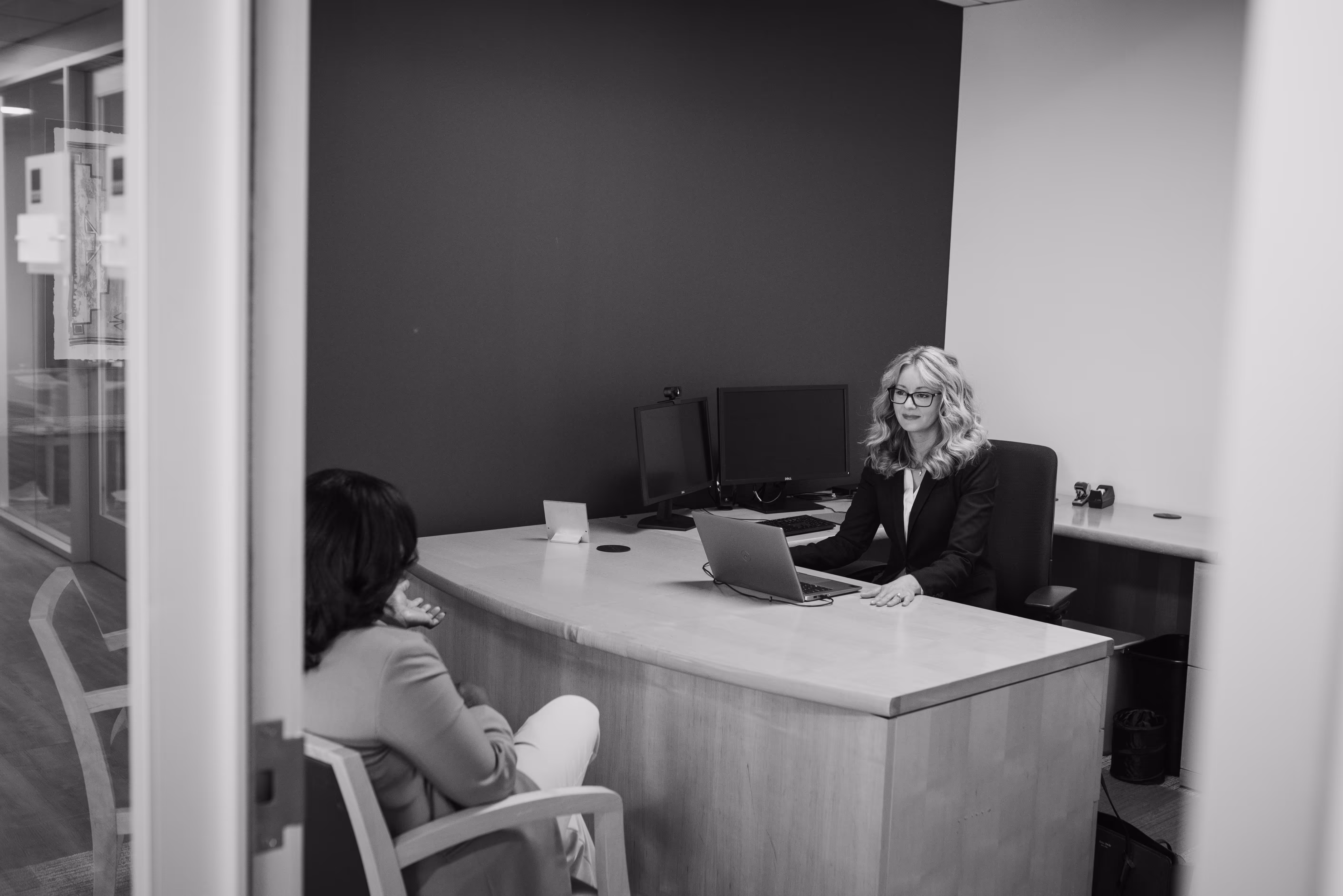 Two women having a professional meeting at a desk in an office, with one using a laptop.
