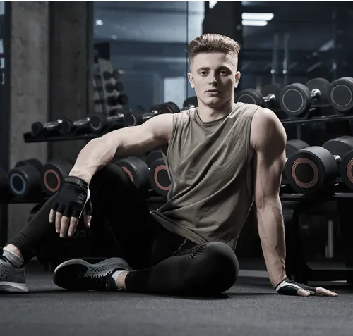 Young man resting on gym floor beside dumbbells.
