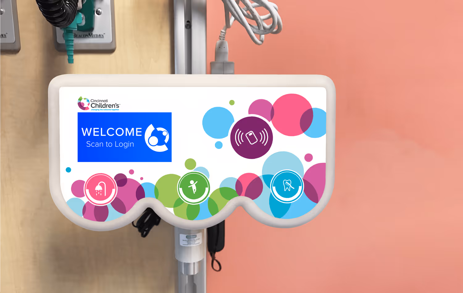 The actual ADL 1-2-3 device in use at a hospital, showing the welcome screen. The device has 3 different colored tap areas with icons indicating each of the daily activities patients need to complete: shower, exercise, and bathe.