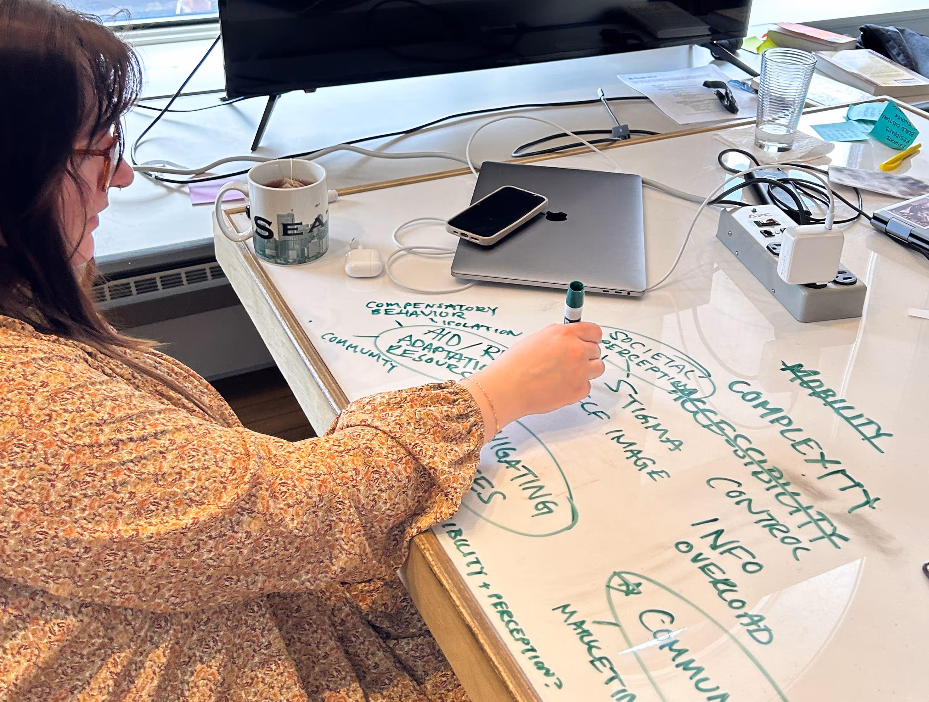 A woman draws a mind map related to BMI with a dry erase marker on a whiteboard table.