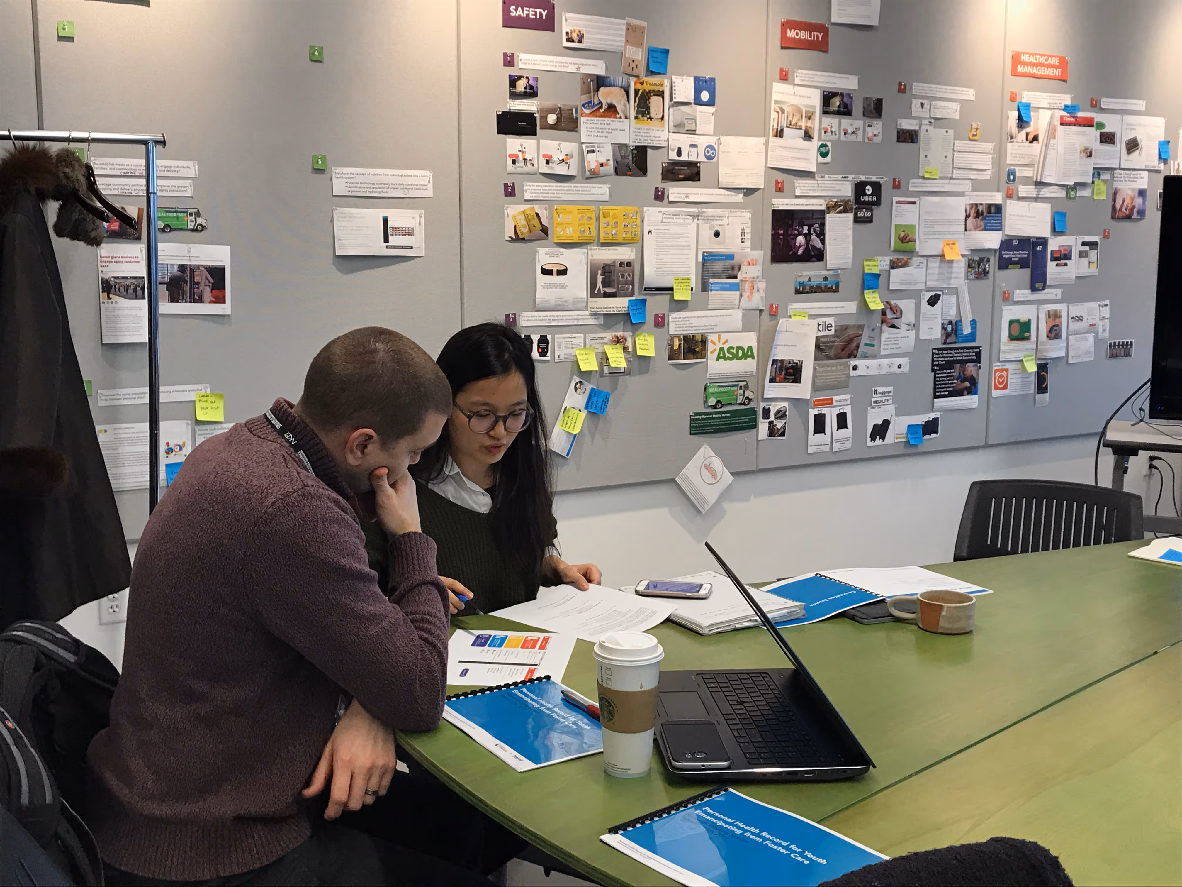 A male stakeholder and female research student sit at a table reviewing research materials.