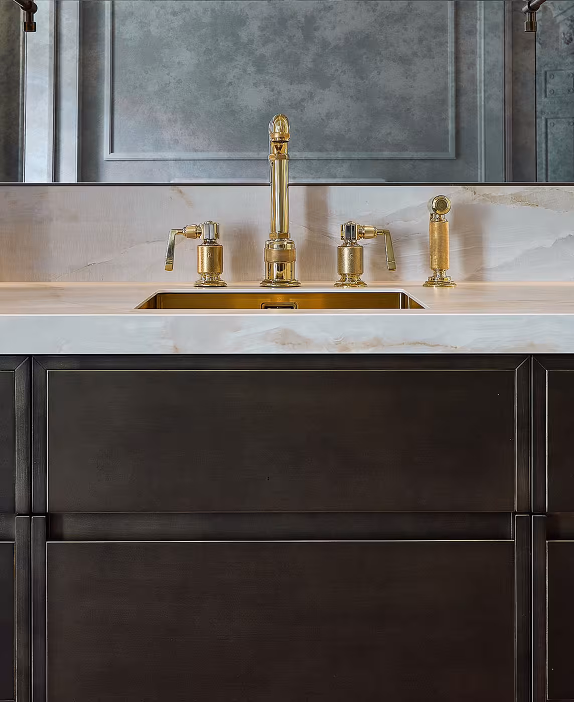 A close up of a gold mixer tap, marble work tops and brown kitchen units.