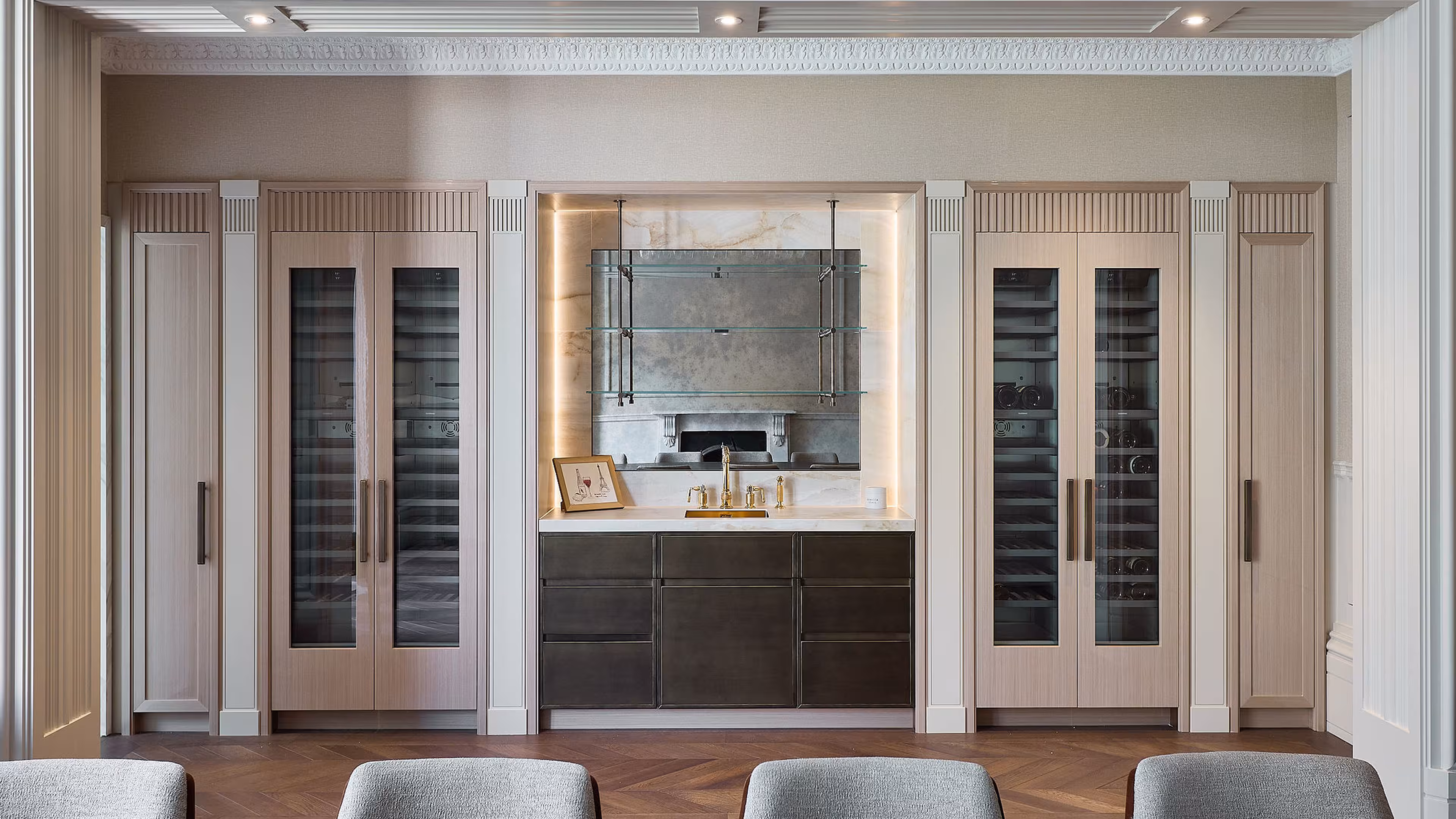 A luxury kitchen showing a gold mixer tap, marble work tops and brown kitchen units, with full height wine coolers either side.