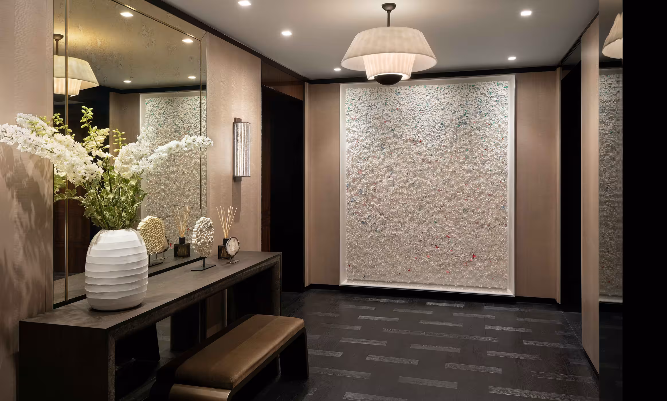 Entrance area with a mirror, sat behind a dark wood table and stool. The far wall has a full height artwork in white.