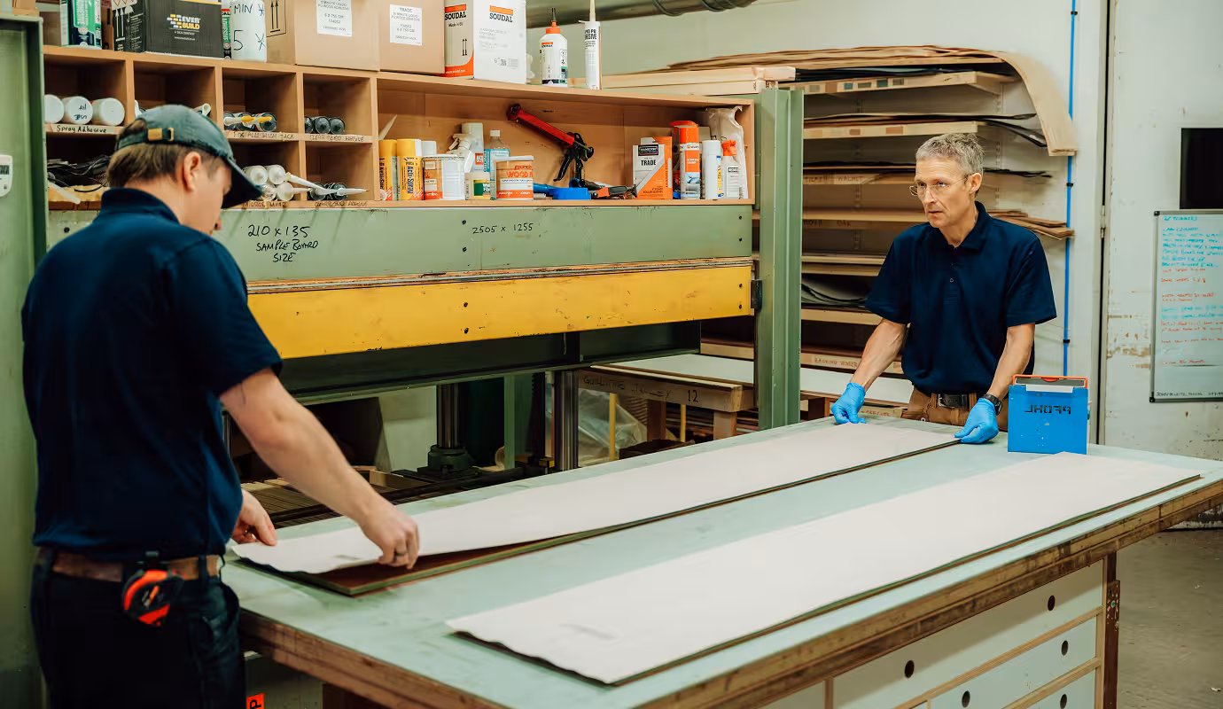 Two men in a workshop either side of a long sample of wooden