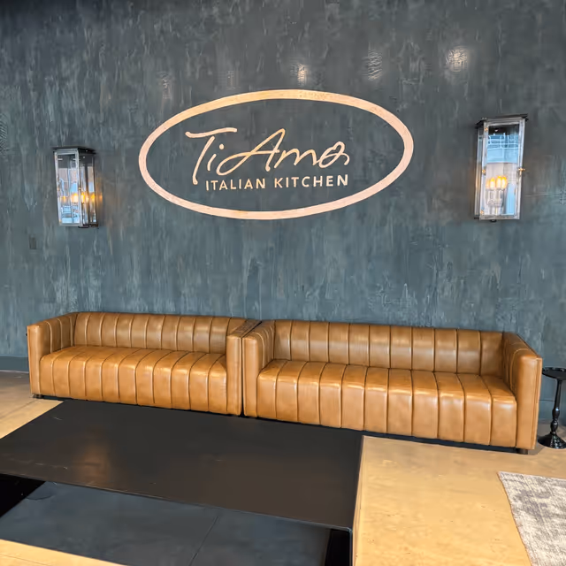Elegant lounge with two brown leather sofas against a dark textured wall, featuring "Ti Amo Italian Kitchen".
