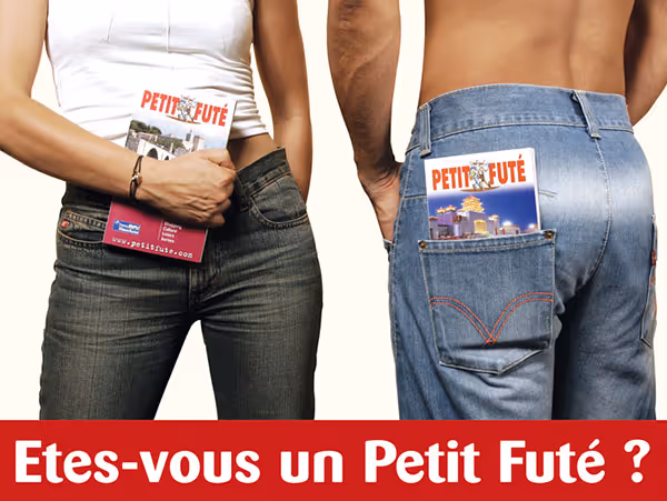 Un homme en débardeur blanc tient un guide du Petit Futé, un homme de dos a aussi un guide Petit Futé dans la poche arrière de son jean, texte en bas : « Etes-vous un Petit Futé ? »