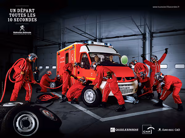 Équipe de pompiers en combinaison rouge effectuant un changement rapide de pneus sur un véhicule de secours rouge dans un garage.