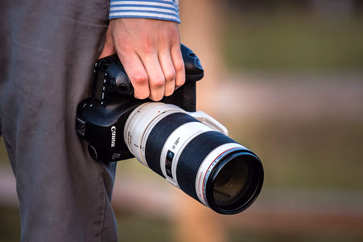 Main tenant un appareil photo Canon avec un objectif téléobjectif blanc 70-300 mm.