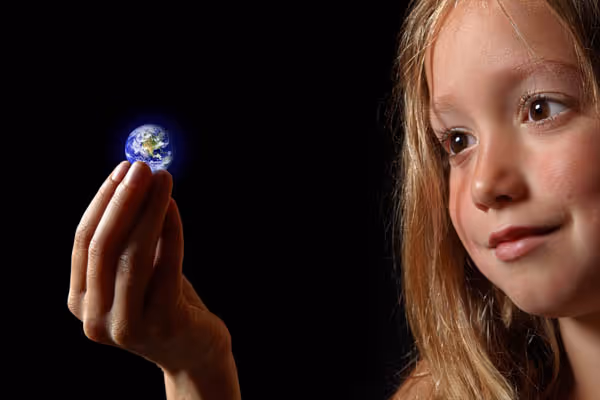 Une fillette aux cheveux blonds tient une petite Terre lumineuse entre son pouce et son index sur un fond noir.