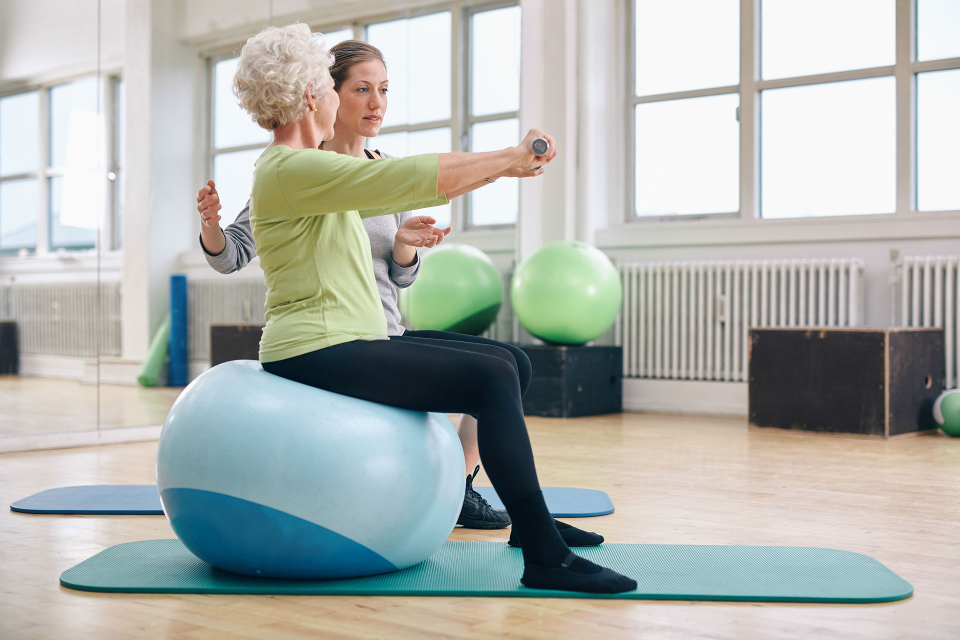 Elderly woman sitting on theraby ball, lifting weights