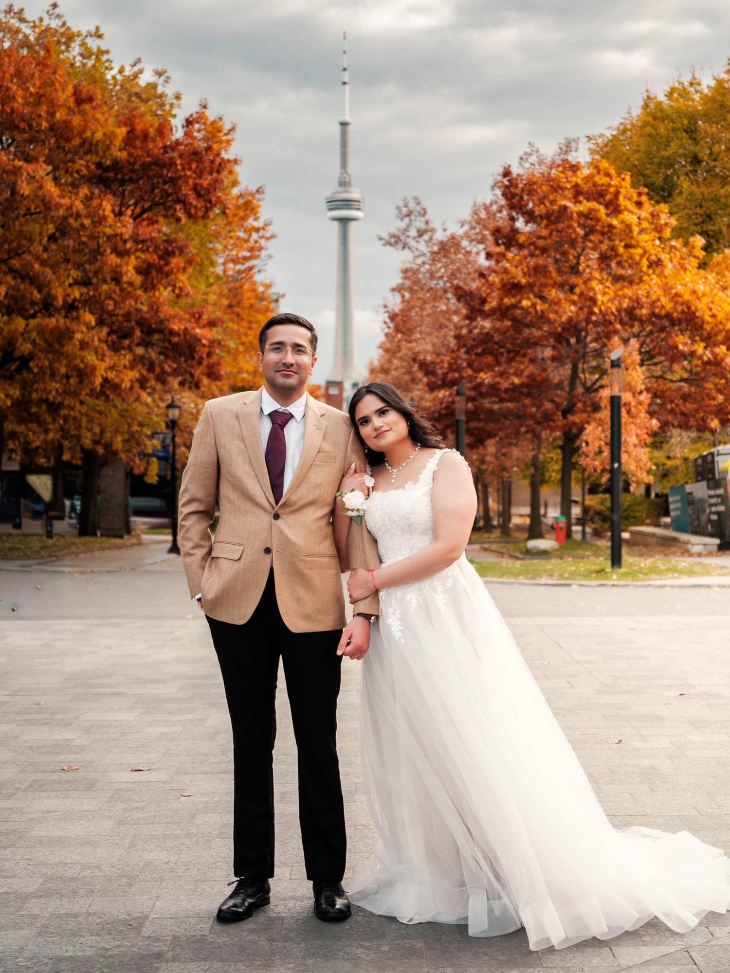 An engaged pre-wedding fall photoshoot with fall colours at University of Toronto's main entrance with a clear view of the CN Tower and Downtown skyline with Kash Klicks Studios