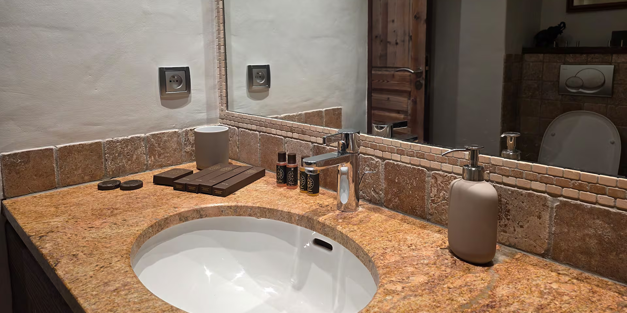 Bathroom countertop with a round white sink, chrome faucet, soap dispenser, and neatly arranged toiletries next to a large mirror.