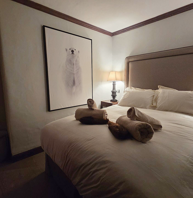 Cozy bedroom with a beige upholstered headboard, white bedding, rolled towels on the bed, a bedside lamp, and a large framed polar bear artwork on the wall.