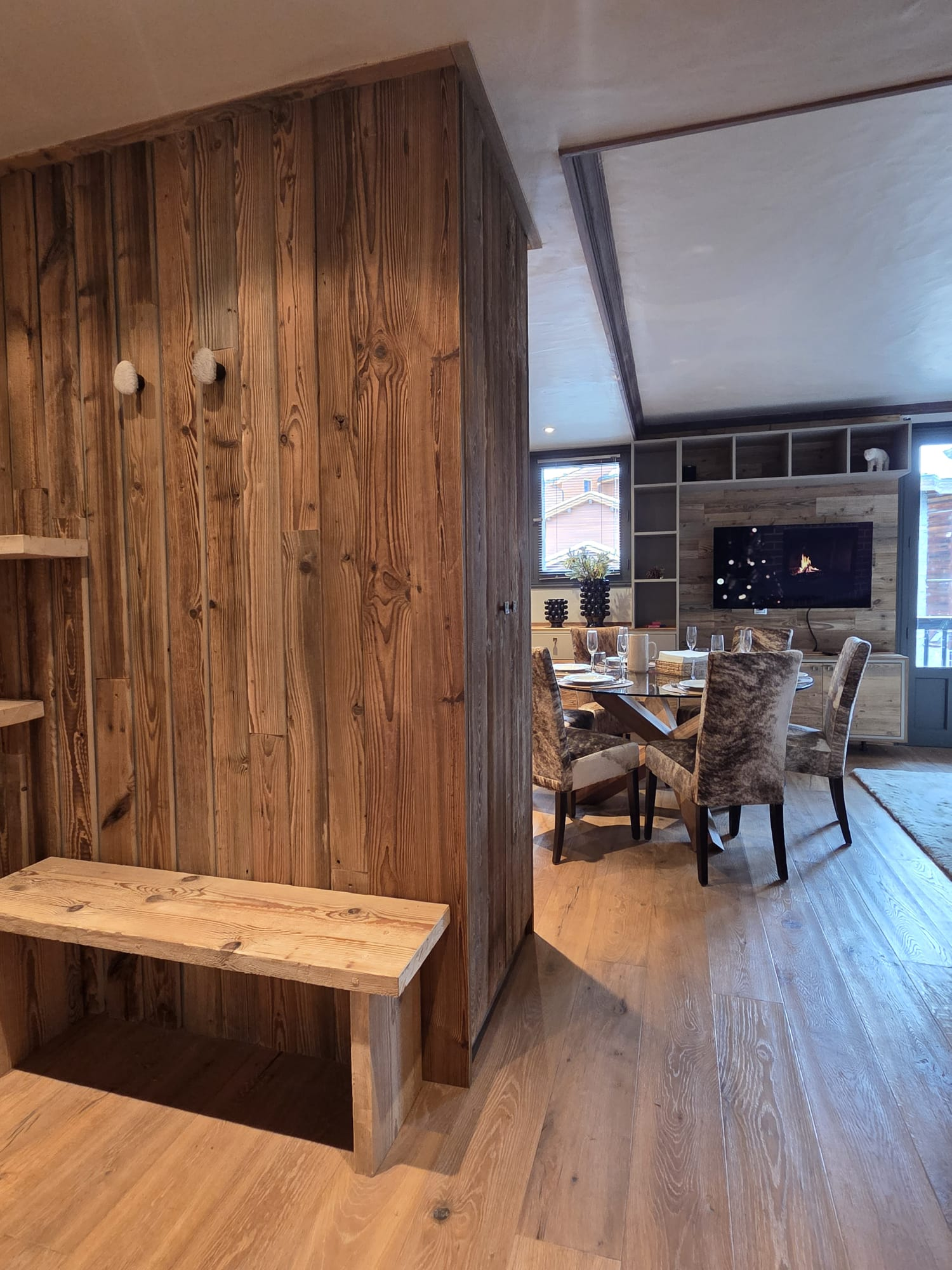 Cozy dining area with wooden floors, a round table set for six with cushioned chairs, and a wall-mounted TV above a fireplace.