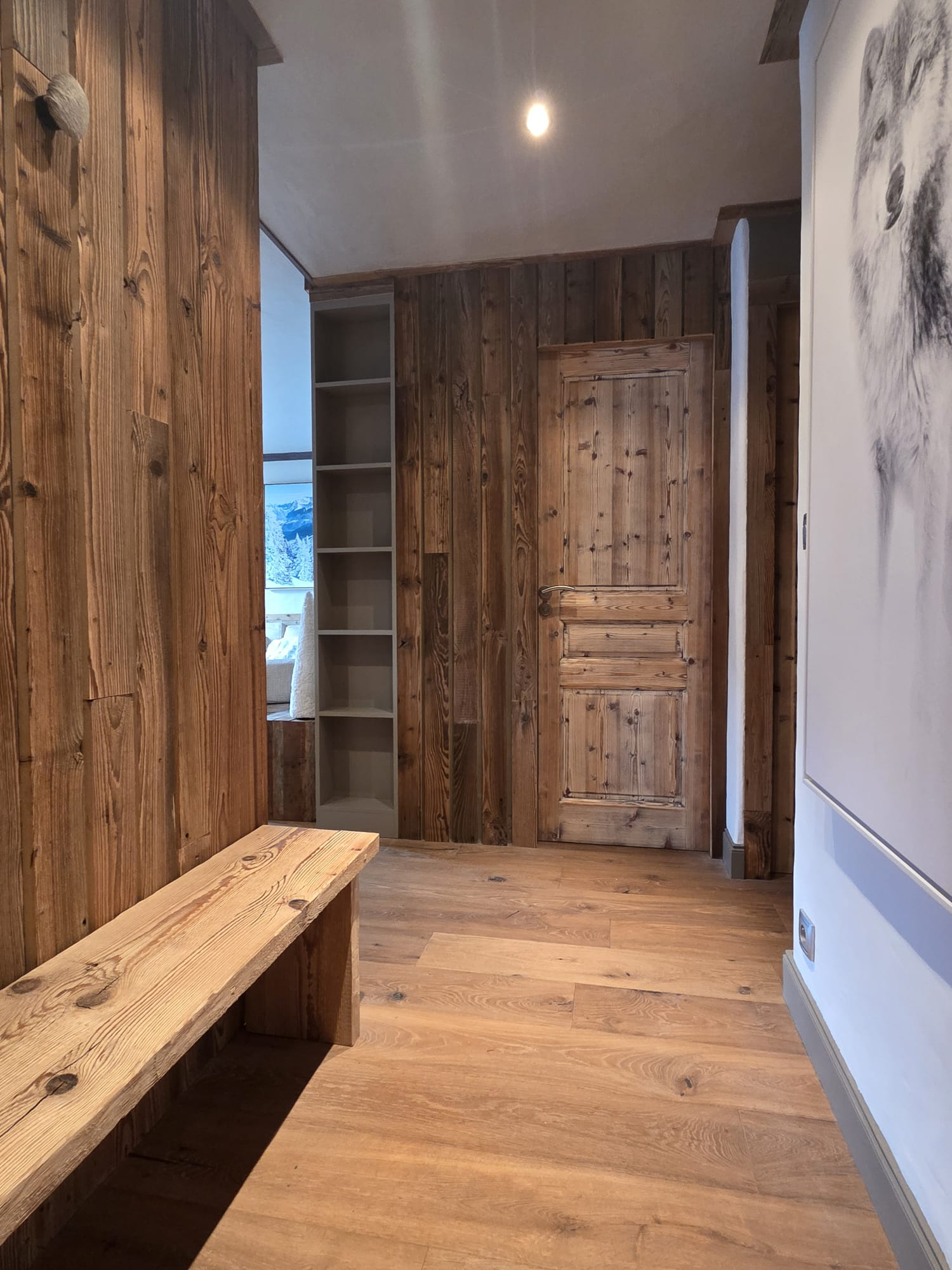Wood-paneled hallway with a wooden door, bench, built-in shelves, and a white wall featuring a wolf painting.