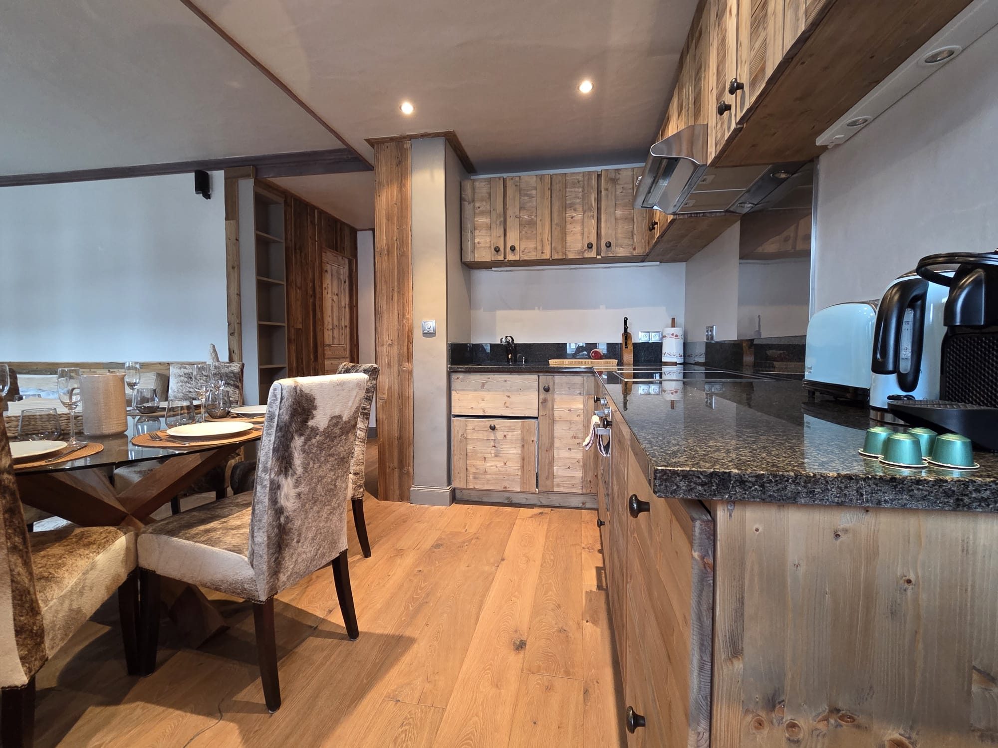 Modern kitchen with wooden cabinets, black granite countertops, and dining area with glass table and upholstered chairs.