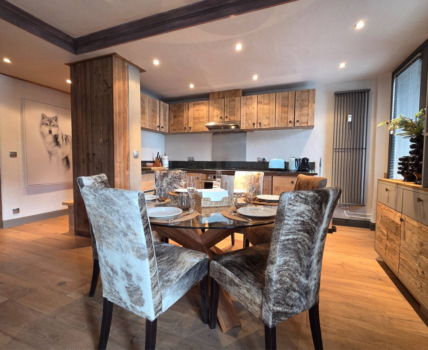 Modern kitchen with wooden cabinets, a glass dining table, and six cowhide-patterned chairs set for a meal.