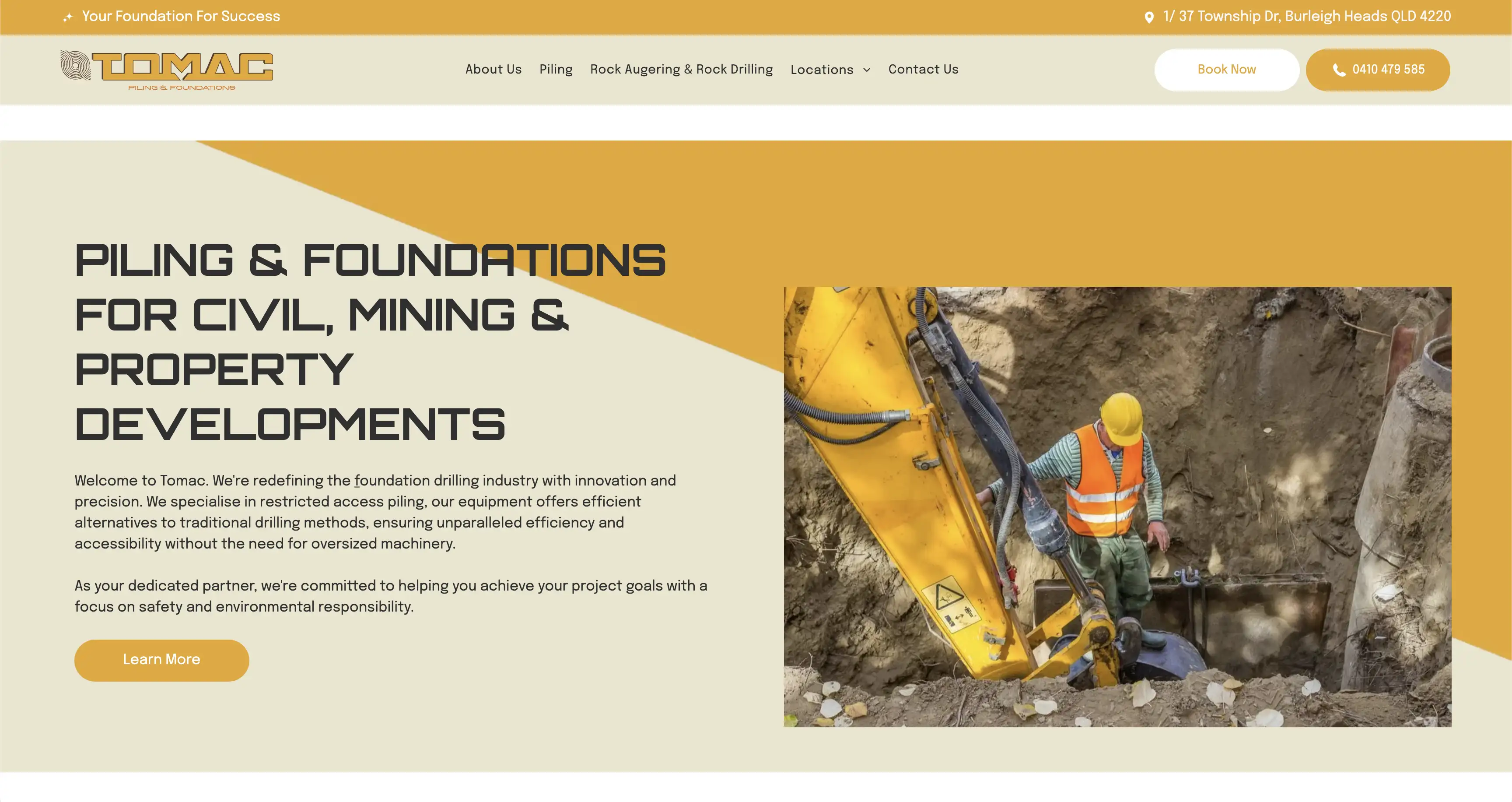 Construction worker wearing a yellow hard hat and orange safety vest operating drilling machinery in a deep excavation site.