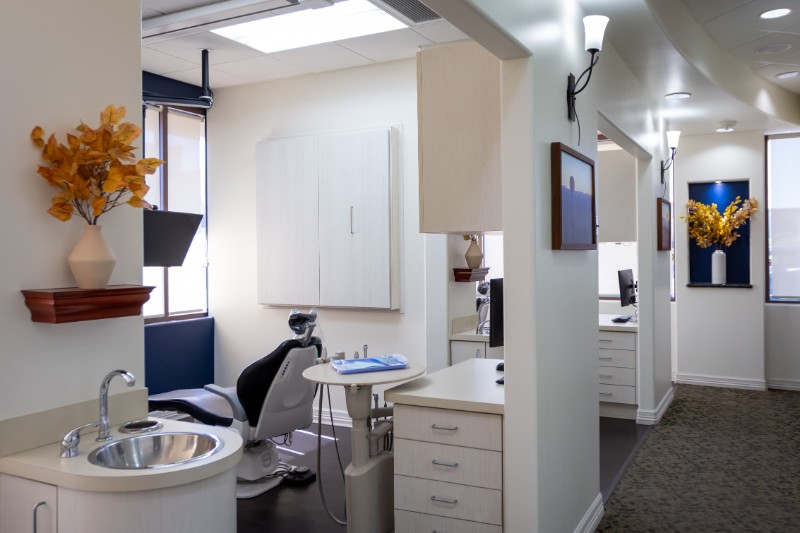 Modern dental clinic with multiple workstations, dental chair, sink, and decorative yellow flowers on walls.