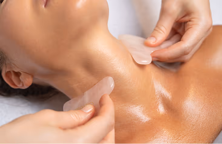 Close-up of a person receiving a gua sha massage on their neck using smooth, flat tools.