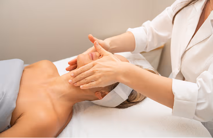 Woman receiving a facial massage while lying on a spa bed with a headband on.